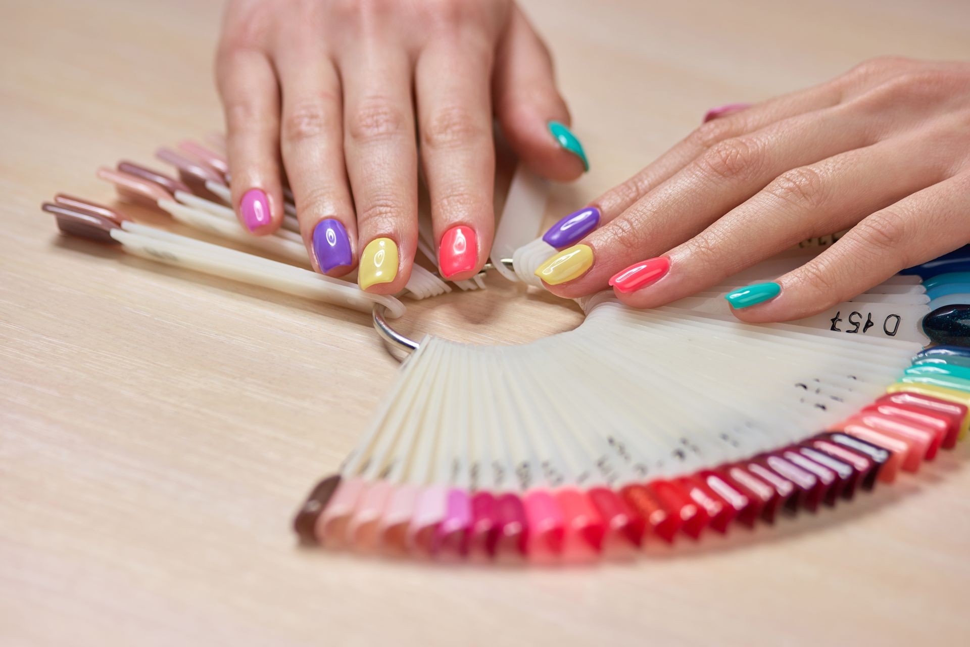 Multicolored summer manicure on female hands. Beautiful pastel manicure on young womans hands, palettes with nail polishes. Salon beauty and spa.